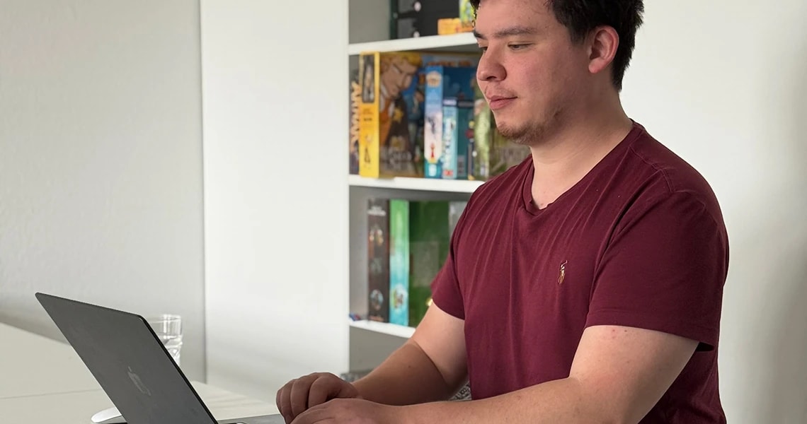 Frank steht am Schreibtisch und arbeitet am Laptop